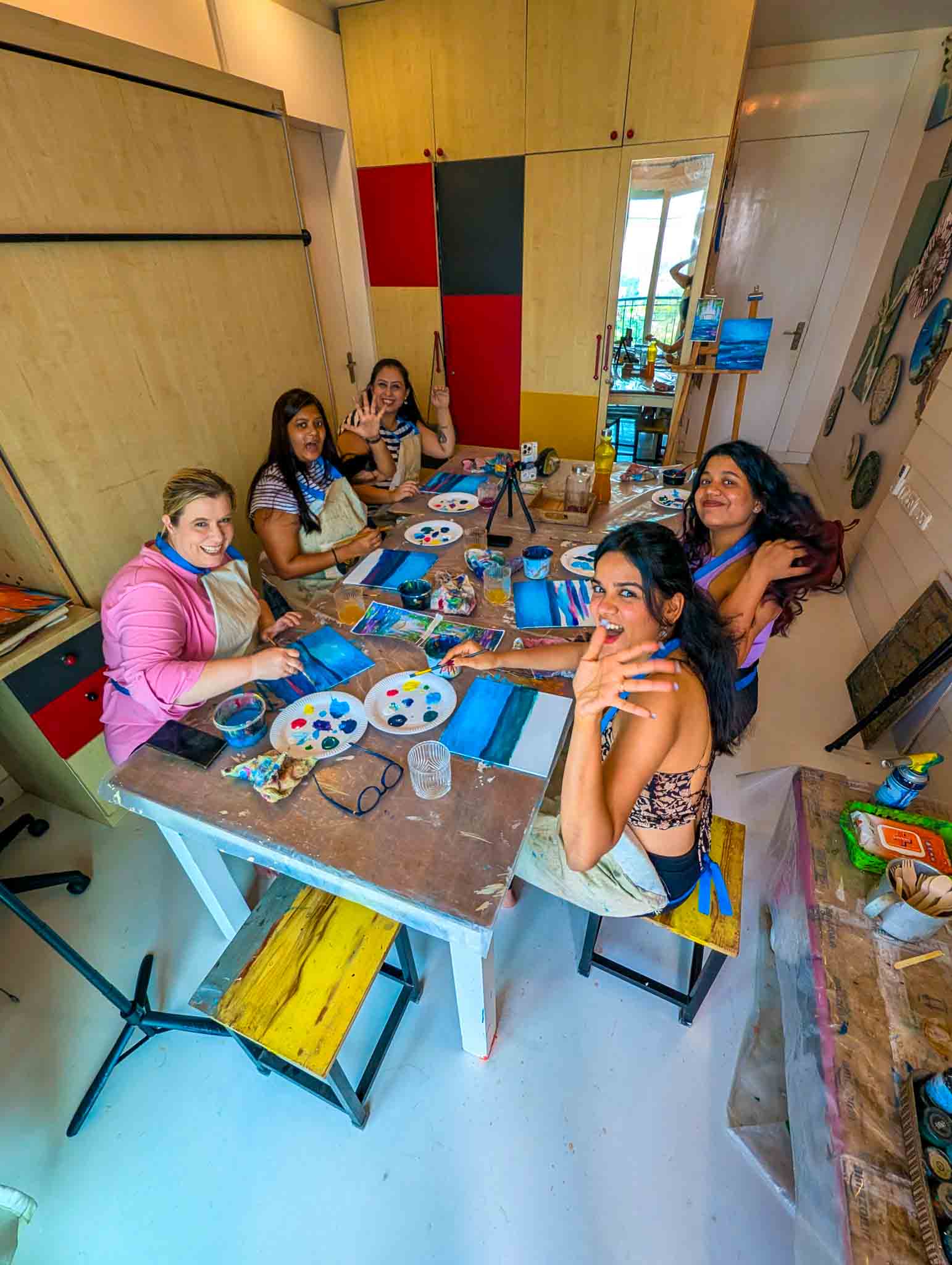 Group of women painting and chatting around a table with colorful paints during a fun and social Sip & Paint experience.